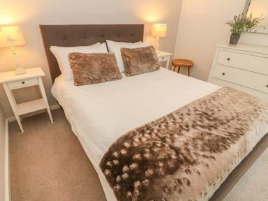 A bedroom with a bed flanked by two lamps and nightstands a stool and a dresser with a plant at The Potting Shed in Burton-in-Kendal near Kirkby Lonsdale
