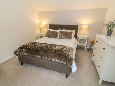 A bedroom with a bed between two lamps and side tables and a white chest of drawers with a plant at The Potting Shed Burton-in-Kendal near Kirkby Lonsdale