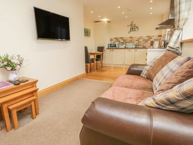 A living area with a sofa and wall mounted TV next to a kitchen and dining table at Snowdrop Cottage in Aldingham