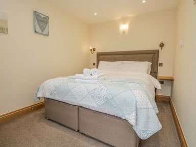 A bedroom with a double bed a patterned quilt and folded towels on the bed at Snowdrop Cottage in Aldingham