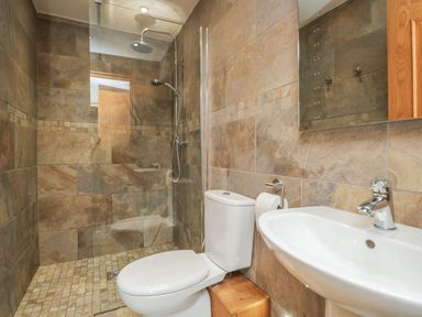 A bathroom with a toilet sink and walk in shower with stone tile walls at Snowdrop Cottage in Aldingham
