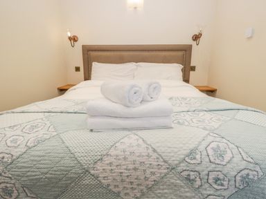 A bed with a padded headboard white pillows white towels and a patterned quilt at Snowdrop Cottage in Aldingham