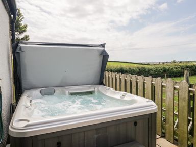 An outdoor hot tub with bubbling water next to a wooden fence and grassy field at Snowdrop Cottage in Aldingham