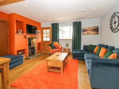 A living room with an orange wall fireplace wooden coffee table blue sofa and green curtains at Bluebell Cottage in Aldingham