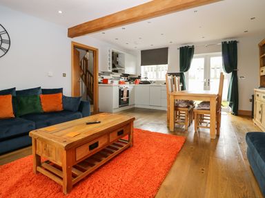 An open living room and kitchen with a wooden dining table and chairs a wooden coffee table and a blue sofa with cushions at Bluebell Cottage in Aldingham