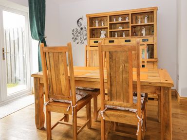 A dining room with wooden table and chairs a wooden cabinet and a glass door with green curtains at Bluebell Cottage in Aldingham