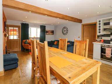 A dining table with chairs in an open plan dining and living area with a blue sofa and orange armchair at Bluebell Cottage in Aldingham