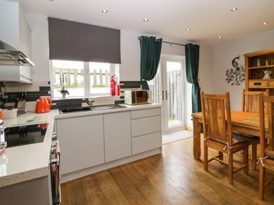 A kitchen with white cabinets a black sink wooden dining table and chairs with orange placemats at Bluebell Cottage in Aldingham