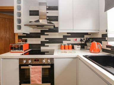 A kitchen with orange toaster kettle and containers on countertops a stove and a black sink at Bluebell Cottage in Aldingham