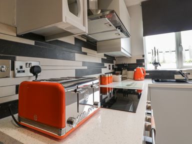A kitchen counter with an orange toaster orange kettle knife set and stovetop at Bluebell Cottage in Aldingham