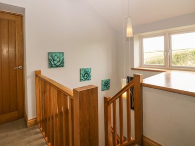 A stair landing with wooden handrails a window and green floral wall art at Bluebell Cottage in Aldingham