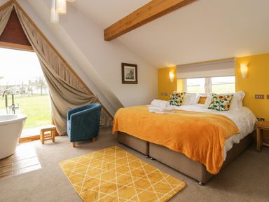 A bedroom with a large bed orange blanket blue chair freestanding bathtub and yellow rug at Bluebell Cottage in Aldingham