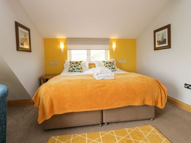 A bedroom with a double bed yellow bedding floral pillows yellow accent wall and framed pictures Bluebell Cottage Aldingham