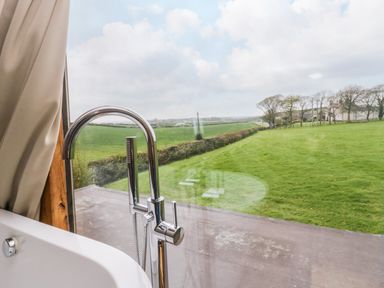 A bathroom with a bathtub and a chrome faucet next to a large window overlooking a grassy field at Bluebell Cottage in Aldingham