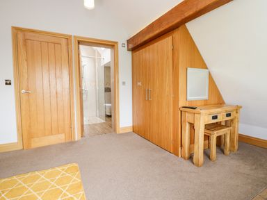 A room with wooden doors a built in wardrobe a wooden dressing table with stool and an open door leading to a bathroom at Bluebell Cottage in Aldingham
