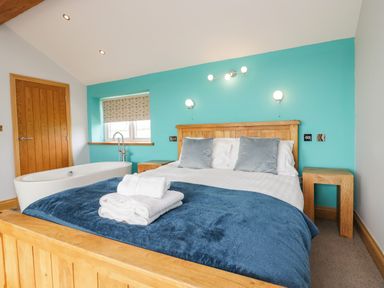 A bedroom with a wooden bed a blue blanket white towels two pillows a bathtub wooden furniture and a turquoise wall at Bluebell Cottage in Aldingham