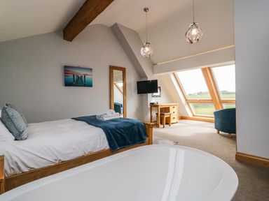 A bedroom with a wooden bed a white bathtub and large windows at Bluebell Cottage in Aldingham
