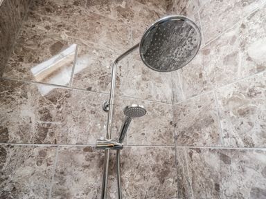 A shower area with a large overhead showerhead and a handheld showerhead on tiled walls at Bluebell Cottage in Aldingham