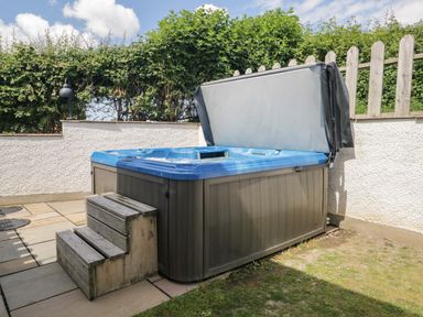 An outdoor hot tub with steps on a patio area next to a white wall and hedge at Bluebell Cottage in Aldingham