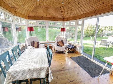 A conservatory with a wooden ceiling a table with chairs two armchairs with footstools and red floor lamps at Teach Teolai in Carraroe County Galway