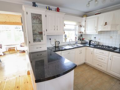 A kitchen with black countertops white cabinets a sink a gas stove and appliances at Teach Teolai in Carraroe County Galway