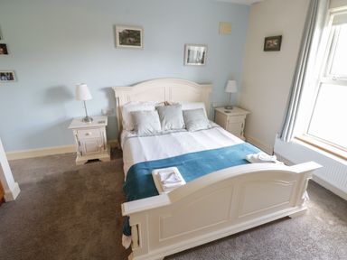 A bedroom with a double bed with pillows and a blue blanket two bedside tables with lamps and framed pictures on the walls at Teach Teolai in Carraroe County Galway