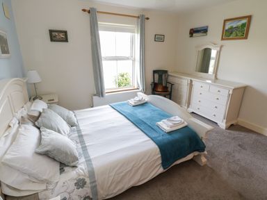 A bedroom with a bed linens and pillows a window with curtains a chair a dresser with mirror and paintings on the wall at Teach Teolai in Carraroe County Galway