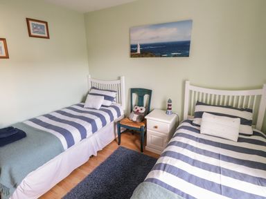 A bedroom with two single beds with striped bedding a nightstand blue chair with owl cushion and ocean view picture at Teach Teolai in Carraroe County Galway