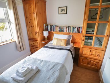 A bedroom with a single bed towels on the bed wooden wardrobes and shelves with books and board games at Teach Teolai in Carraroe County Galway