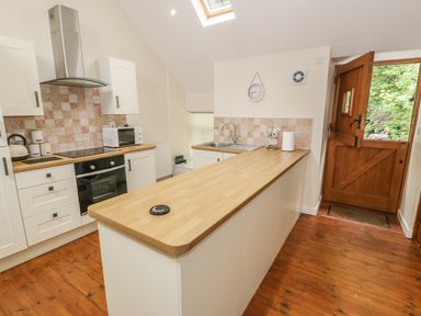 A kitchen with a wooden countertop white cabinets a stove microwave sink wooden door and tiled backsplash at Hendoll Cottage 2 Fairbourne near Dolgellau