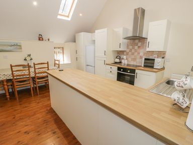 A kitchen with wooden floor a dining table with four chairs and a long countertop at Hendoll Cottage 2 Fairbourne near Dolgellau