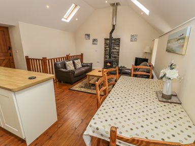 An open living and dining room with a dining table and chairs a wood stove leather sofas and wooden floors at Hendoll Cottage 2 Fairbourne near Dolgellau