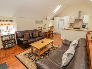 An open living room and kitchen with two leather sofas a wooden coffee table a dining table with chairs and kitchen cabinets at Hendoll Cottage 2 Fairbourne near Dolgellau