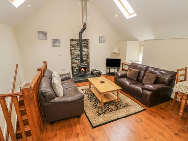 A living room with two brown sofas a wood stove a wooden coffee table and skylights at Hendoll Cottage 2 Fairbourne near Dolgellau