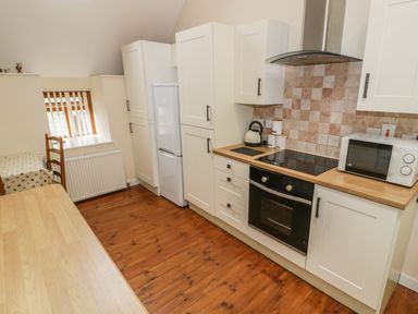 A kitchen with white cabinets wooden countertops a stove oven microwave and kettle at Hendoll Cottage 2 Fairbourne near Dolgellau