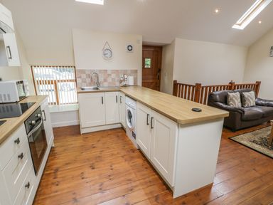 A kitchen with white cabinets wooden countertops and a brown leather sofa in an adjacent room at Hendoll Cottage 2 Fairbourne near Dolgellau