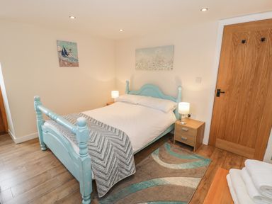 A bedroom with a double bed blue bed frame wooden floor and bedside tables with lamps at Hendoll Cottage 2 Fairbourne near Dolgellau