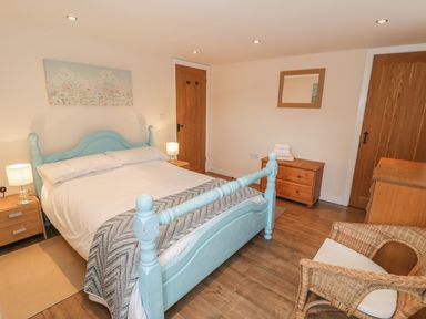 A bedroom with a blue bed frame wooden furniture and a wicker chair at Hendoll Cottage 2 Fairbourne near Dolgellau