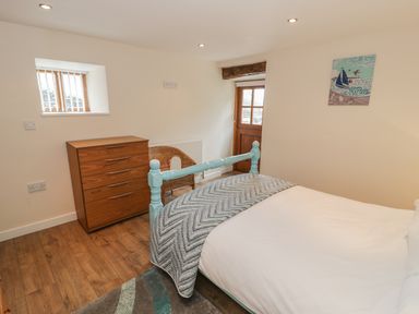 A bedroom with a wooden chest of drawers a wicker chair a bed with a blue frame and a wooden door at Hendoll Cottage 2 Fairbourne near Dolgellau