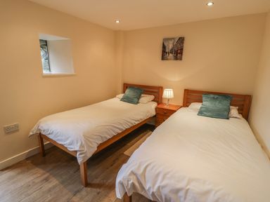 A bedroom with two single beds a wooden nightstand and a lamp at Hendoll Cottage 2 Fairbourne near Dolgellau