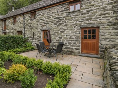 A stone cottage exterior with wooden doors a patio table and chairs and green shrubbery at Hendoll Cottage 2 Fairbourne near Dolgellau