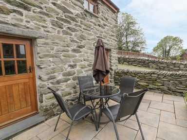 An outdoor patio with a round glass table four chairs and a closed umbrella next to a stone wall at Hendoll Cottage 2 Fairbourne near Dolgellau
