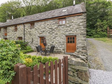 An outdoor patio area with table and chairs in front of a stone cottage with wooden doors and windows at Hendoll Cottage 2 Fairbourne near Dolgellau