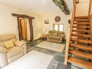 A living room with beige armchairs wooden staircase and stone floor at Hendoll Barn Friog near Fairbourne