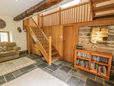 A sitting area with a sofa, staircase, bookshelf, and stone wall at Hendoll Barn in Friog near Fairbourne