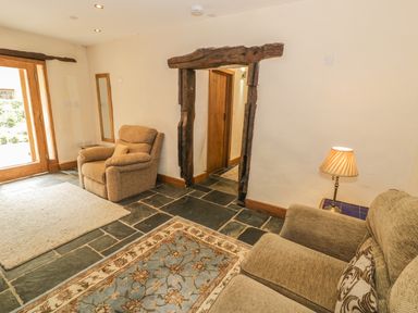 A sitting room with two armchairs a floor lamp and a wooden doorway at Hendoll Barn in Friog near Fairbourne