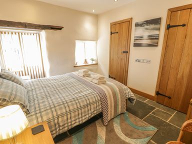 A bedroom with a double bed with checked bedding towels on bed two wooden doors and a small window at Hendoll Barn in Friog near Fairbourne