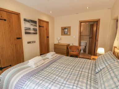 A bedroom with a double bed, two wooden doors, a dresser, a wicker chair, and an en suite bathroom at Hendoll Barn Friog near Fairbourne