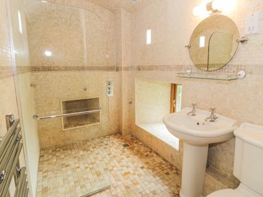 A bathroom with a walk-in shower a pedestal sink a round mirror and a toilet at Hendoll Barn in Friog near Fairbourne