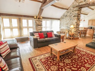A living room with leather sofas a wooden coffee table and a patterned rug at Hendoll Barn in Friog near Fairbourne